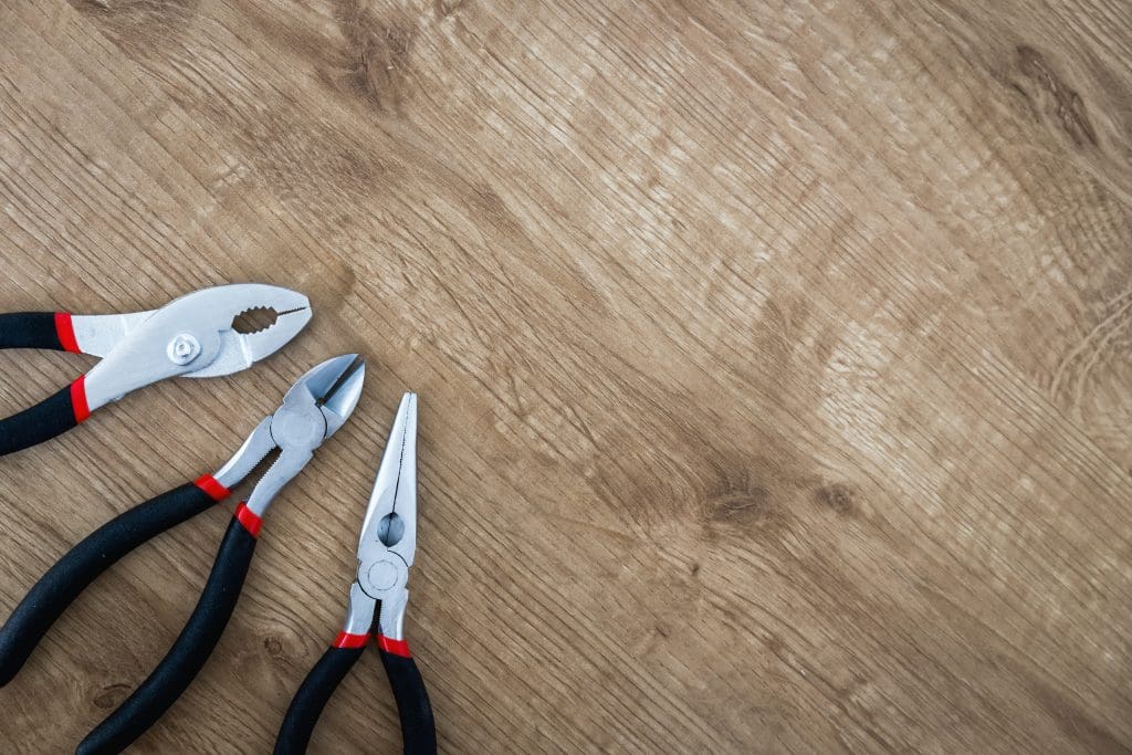 Pliers and other tools sitting against a wood background