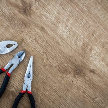 Pliers and other tools sitting against a wood background