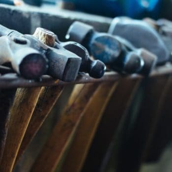 Various hammers hanging in a row from a shelf