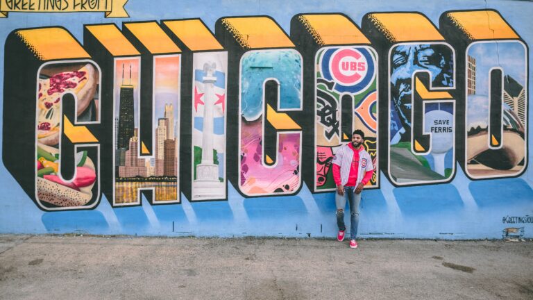 A person standing in front of street art reading "Greetings from Chicago"