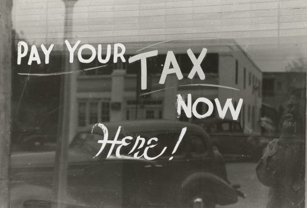 The words "Pay your tax now here!" written on a window