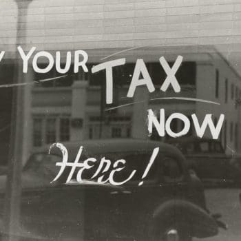 The words "Pay your tax now here!" written on a window