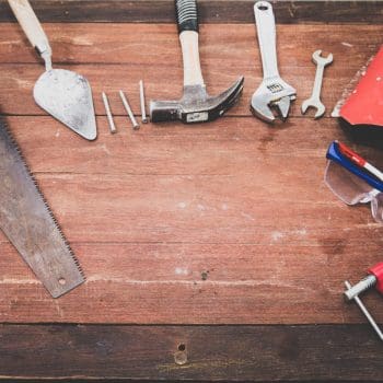 A wrench, hammer, saw, and various other tools atop a wooden table