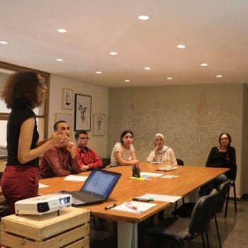 Six people sitting in a meeting room listening to a presentation