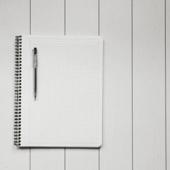 An open spiral notebook with a black pen sitting on top