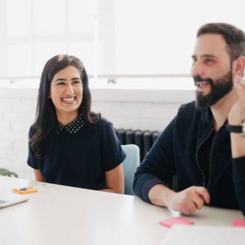 A male and female coworker sitting at a desk smiling and laughing