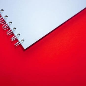 Close-up of the edge of a white spiral notebook against a red background