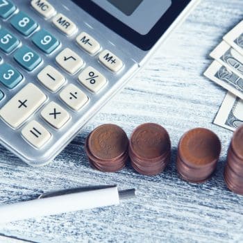 Pennies and $100 bills stacked next to a calculator