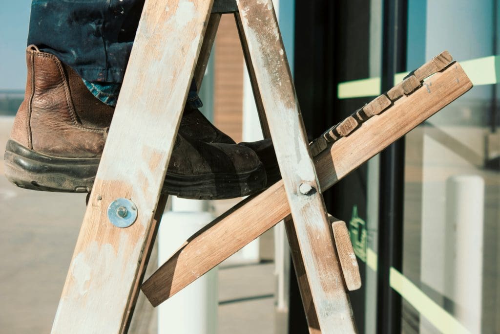 A close up of a handyman climbing a wooden ladder